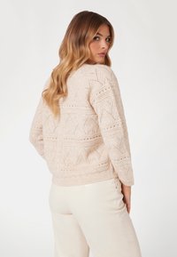 Maglione lavorato a maglia di un delicato rosa chiaro con un motivo geometrico testurizzato, maniche lunghe e orlo a coste. Abbinato a pantaloni di colore crema.