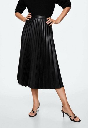 Jupe midi en simili cuir plissé noir avec une taille lisse et une silhouette fluide. Portée avec des talons noirs à lanières.