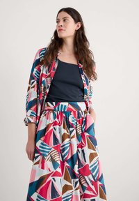 Vícebarevný outfit se vzorovaným sakem a odpovídající sukní. Tkaniny jsou lehké s odvážnými geometrickými tvary v růžové, modré a hnědé barvě.