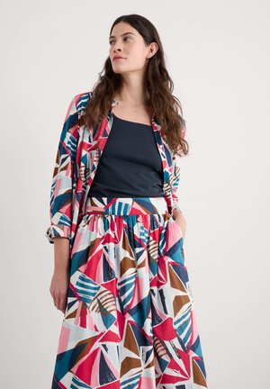Conjunto multicolorido que presenta un blazer estampado y una falda a juego. Las telas son ligeras con formas geométricas audaces en rosa, azul y marrón.