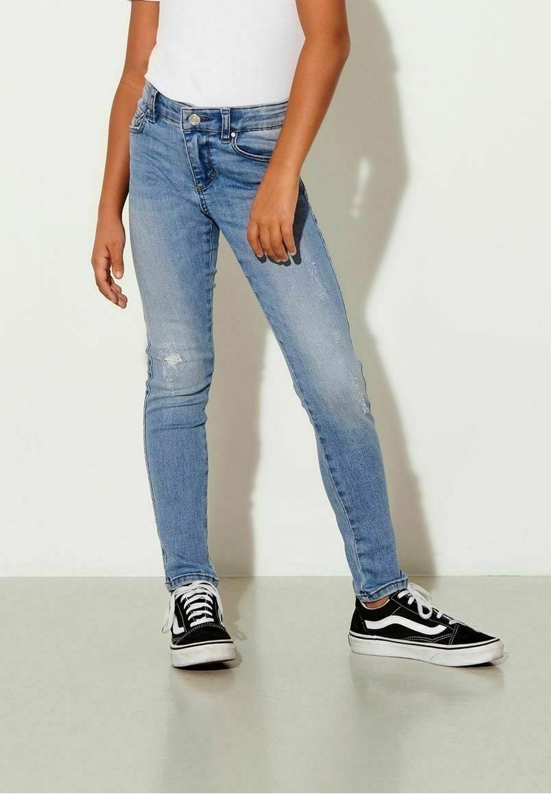 Jeans skinny de denim azul claro con ligero desgaste, que cuentan con un diseño de cinco bolsillos y un cierre de botón. Llevados con zapatillas negras.