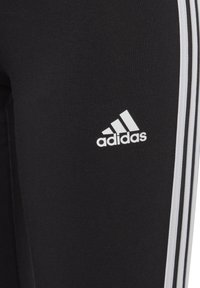 Leggings sportivi neri con texture a costine, logo Adidas bianco e tre strisce verticali bianche lungo il lato.