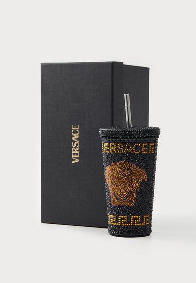 Black cup with rhinestone embellishments, featuring a golden Versace logo and a lion head design, accompanied by a silver straw and black box.