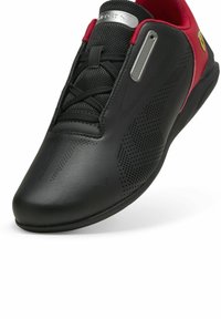 Sort atletisk sko med røde accenter, lavet af glat læder og mesh. Har perforeret design og en slank, afrundet tåform.