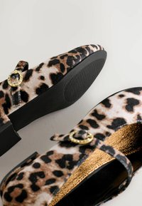 Ballerines à imprimé léopard avec une texture en velours, semelle en synthétique noire et accent de boucle. La doublure intérieure dorée apporte un contraste au design.