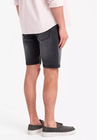 Shorts en denim gris avec un ourlet roulé, design cinq poches et coutures visibles, associés à des chaussures en toile grises et une chemise claire.