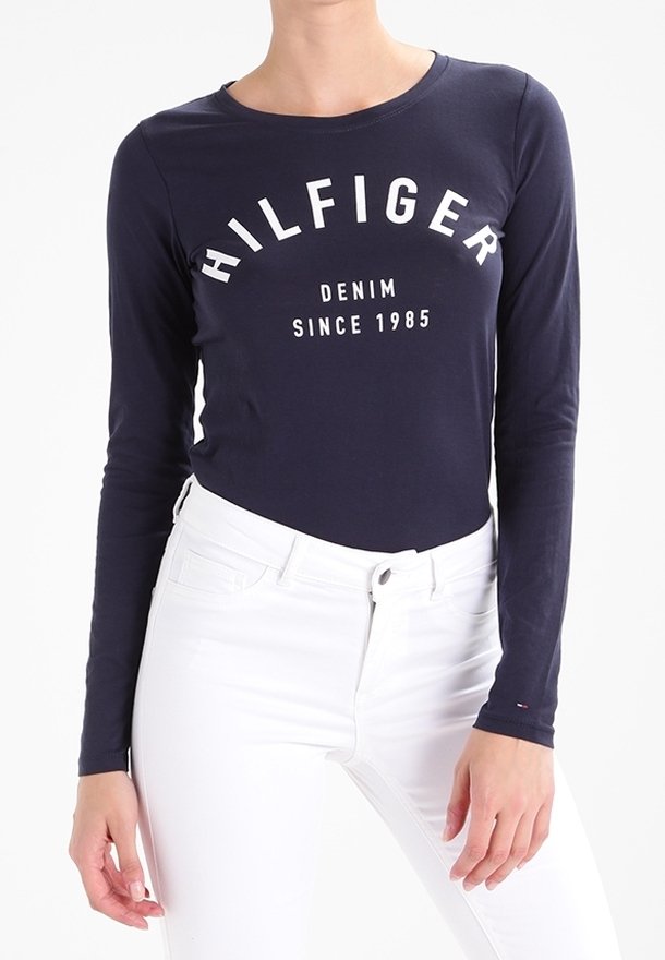 Námořnické tričko s dlouhým rukávem s nápisem "HILFIGER DENIM SINCE 1985" v bílé barvě. Vyrobeno z měkkého materiálu, má kulatý výstřih a přiléhavý střih.