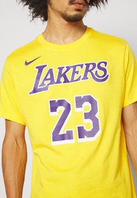 Gul bomullst-shirt med texten "LAKERS" i lila och "23" i en fet design, med Nike-logotyp i lila på vänster axel.