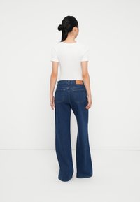 Jeans širokih nogavica od plavog denima s visokim strukom, sa dva stražnja džepa i smešnim kožnim oznakom na struku. Bijela majica s kratkim rukavima.