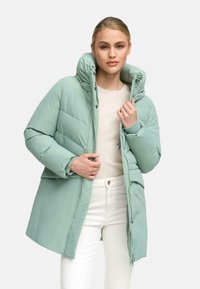 Gaiši zaļš pūkains jaciņa ar augstu apkakli, pogu priekšpusi, quilted rakstu un sānu kabatām, uzvilkts pāri krēmkrāsainai korsetei un baltām biksēm.