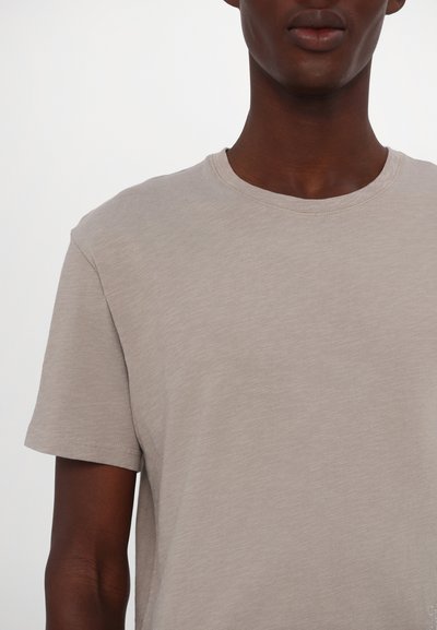 Ljus beige t-shirt med kort ärm och rundad halsringning i mjukt, texturerat tyg. Minimalistisk design utan synliga mönster eller accenter.