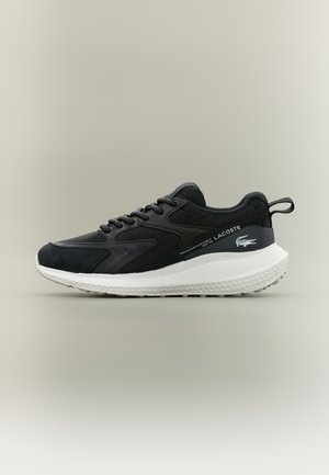 Μαύρο sneaker Lacoste με λευκή χοντρή σόλα, σχέδιο με κορδόνια, και λογότυπο της εταιρείας στη πλευρά και στο πίσω μέρος, πάνω σε ουδέτερο φόντο.