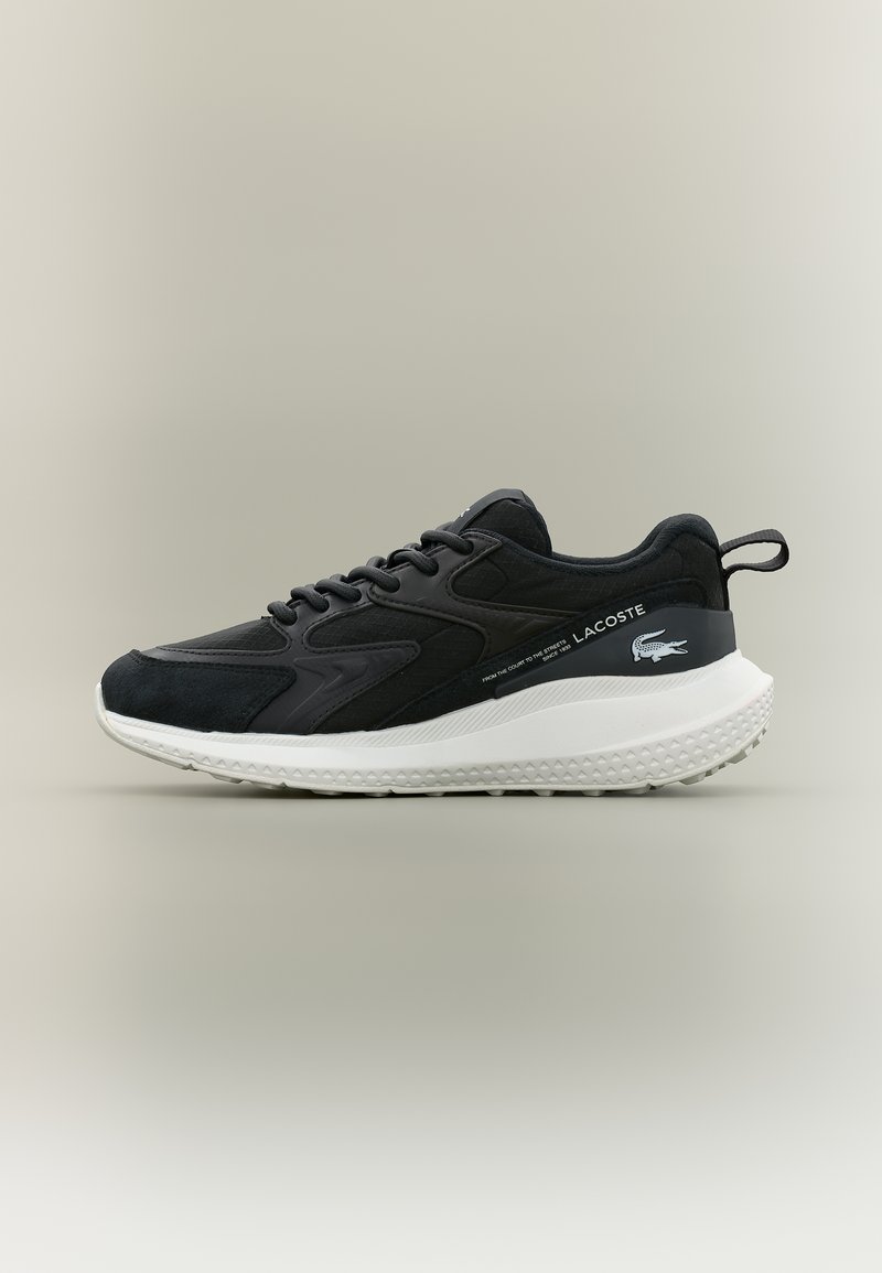 Μαύρο sneaker Lacoste με λευκή χοντρή σόλα, σχέδιο με κορδόνια, και λογότυπο της εταιρείας στη πλευρά και στο πίσω μέρος, πάνω σε ουδέτερο φόντο.
