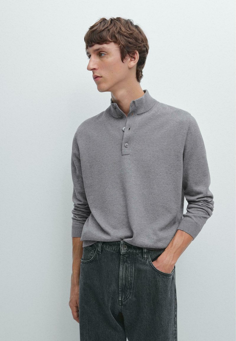 Grå långärmad henley-tröja med knappslå, tillverkad av mjukt material, kombinerad med mörka jeans, med en avslappnad passform och ribbade ärmslut.