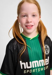 Sort og grøn sportstrøje med lodrette striber; "hummel"-logo tydeligt vist. Har korte ærmer og rund halsudskæring.