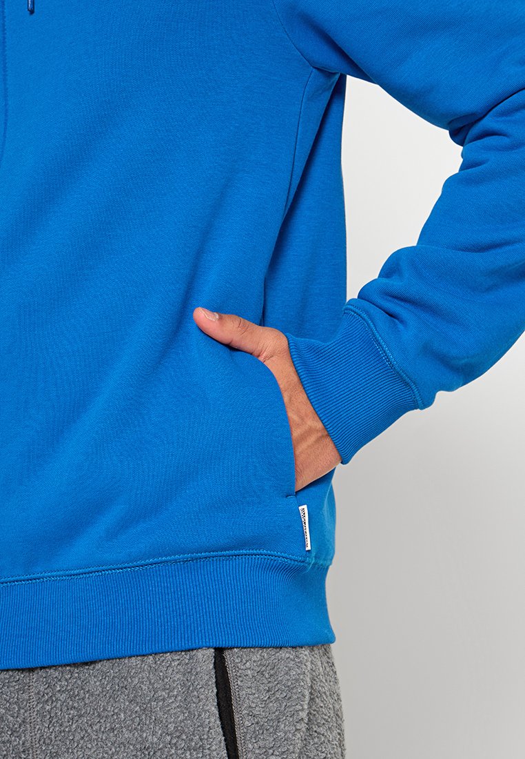 Sweatshirt bleu à manches longues, avec des poignets côtelés et une poche avant, fabriqué à partir d'un tissu texturé. Présenté sur un fond neutre.