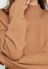 Maglione a collo alto marrone a coste con un design testurizzato, maniche aderenti e un materiale lavorato a maglia morbido. Mette in risalto l'aspetto accogliente del maglione.