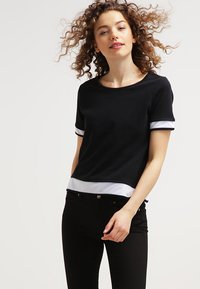 Top nero a maniche corte con dettagli in rete bianca sui polsini e sull'orlo, caratterizzato da un collo rotondo e una vestibilità rilassata. Tessuto di texture liscia.