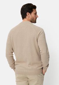 Beige knit sweater with a round neckline, raglan sleeves, and ribbed cuffs and hem, featuring a soft texture and minimal detailing.
