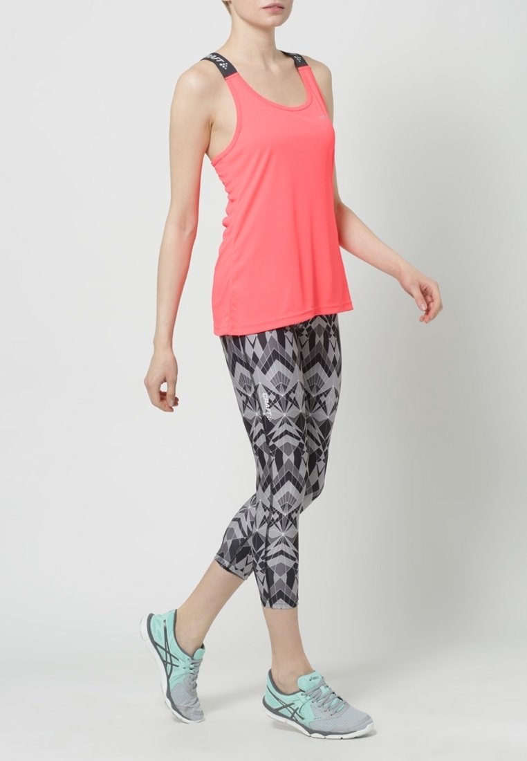 Světlé růžové sportovní tílko s černými ramínky, kombinované s černými a šedými legínami se vzorem a světle modrými běžeckými botami.