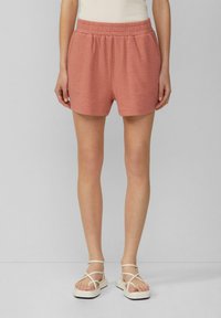 Korallenrosa, strukturierte Stoffshorts mit elastischem Bund, kombiniert mit weißen Sandalen mit Riemchen.