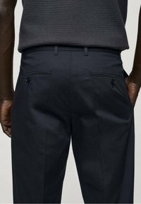 Tmavě námořnické kalhoty s poutky na pásek, bočními kapsami a dvěma zadními kapsami s knoflíkovými zapínáními. Hladký materiál a střih na míru.
