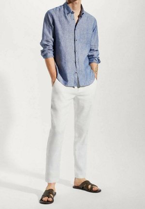 Světle modrá košile na knoflíky z lněné látky, kombinovaná s bílými zúženými kalhotami a hnědými sandály na pásky. Minimalistický design s detailem kapsy.