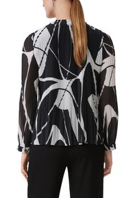 Czarna i biała plisowana bluzka z długimi przezroczystymi rękawami, zdobiona abstrakcyjnymi wzorami i okrągłym dekoltem. Materiał wydaje się lekki i zwiewny.