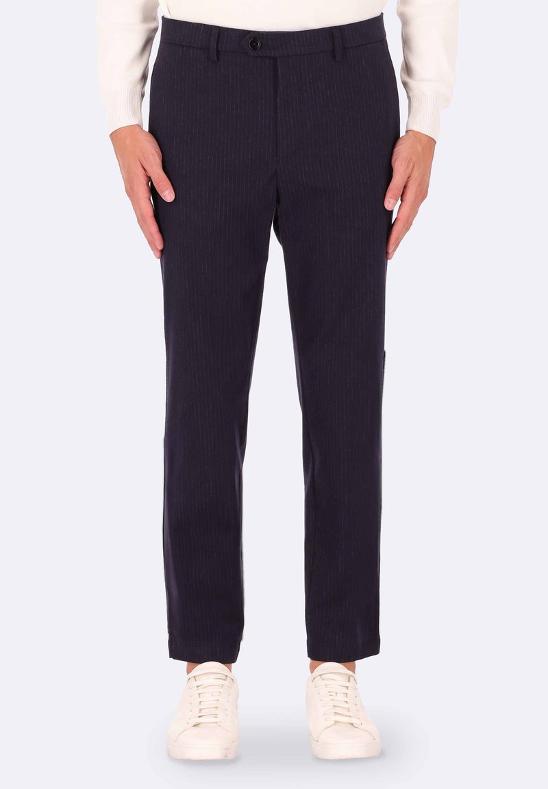 Pantaloni a righe navy con vestibilità slim, dotati di chiusura a bottoni e tasche laterali, abbinati a sneaker bianche. Tessuto morbido.