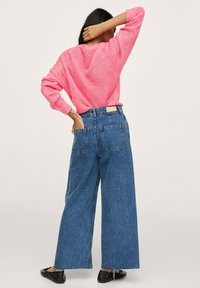 Vaaleanpunainen neulepaita, jossa on rento malli ja joustavat hihat, yhdistettynä korkeavyötäröisiin, leveälahkeisiin sinisiin farkkuihin, joissa on takataskut.