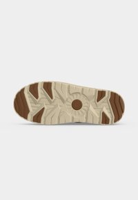Semelle de botte en caoutchouc beige et marron avec des crampons profonds multidirectionnels et un motif circulaire au centre pour la traction.