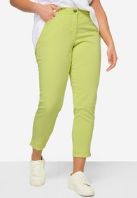 Grüne Baumwollmischung-Caprihosen mit tailliertem Schnitt. Ausgestattet mit Fronttaschen und einem Knopfverschluss, kombiniert mit weißen Sneakers.