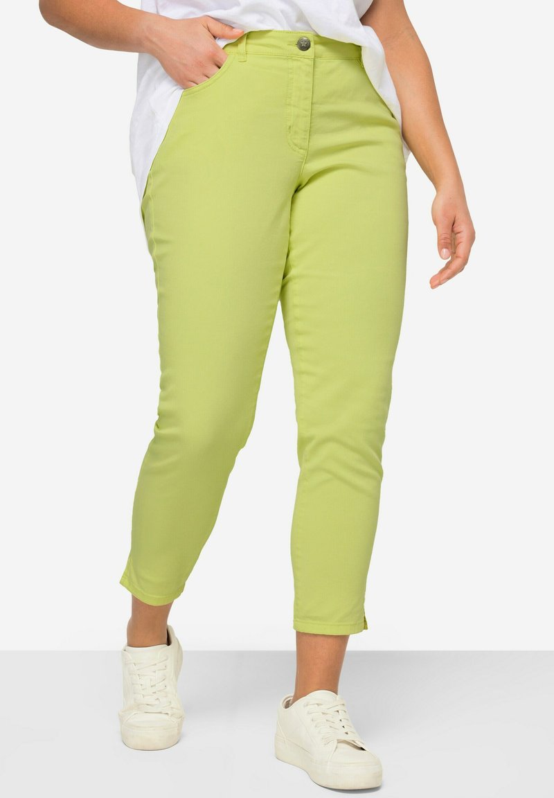 Grüne Baumwollmischung-Caprihosen mit tailliertem Schnitt. Ausgestattet mit Fronttaschen und einem Knopfverschluss, kombiniert mit weißen Sneakers.
