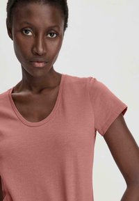 Lyhythihainen t-paita pehmeästä vaaleanpunaisesta kankaasta, jossa on pyöreä pääntie, sileä pinta ja minimaaliset ompeleet hihoissa ja helmassa.