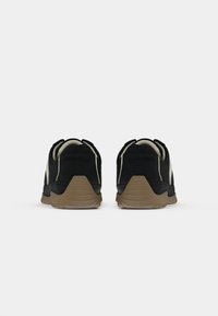 Pair of black and beige sneakers with brown soles viewed from the back on a plain white background.