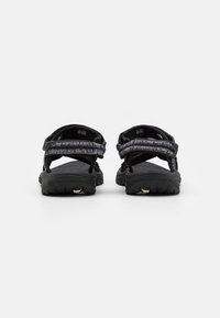 Black sandals feature textured straps with a patterned accent, adjustable closure, and durable rubber soles with grip details.