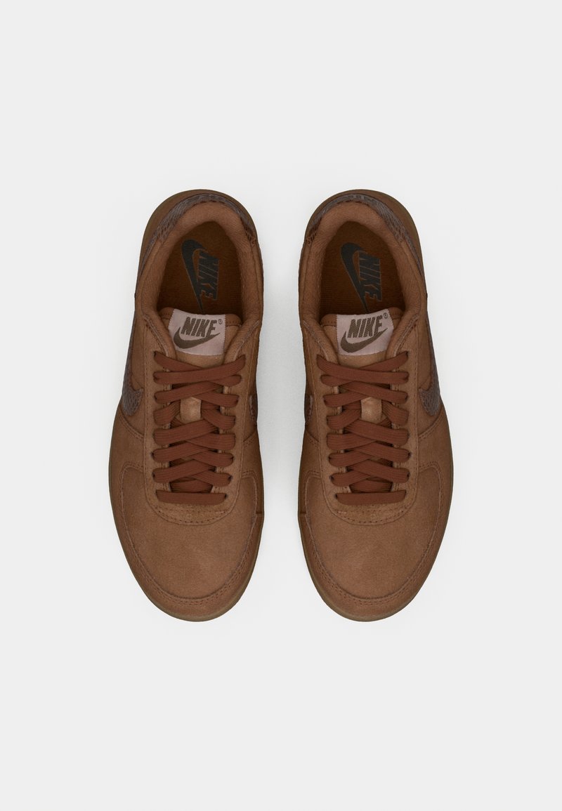 Nike Sneaker aus braunem Wildleder mit passenden Schnürsenkeln. Verfügt über eine glatte Textur, eine abgerundete Spitze und ein schwarzes Logo auf der Zunge und an der Seite.