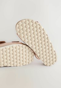 Vaaleanpunaiset kengät, joissa on teksturoitu beige kumipohja, jossa on heksagonaalinen kuvio. Päällinen on sileä, ja siinä on remmiyksiköitä.