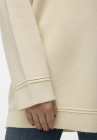Sweat-shirt couleur crème avec une texture douce, doté d'un poignet en côte et de deux lignes de couture horizontales à l'ourlet et à la manche.