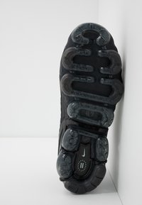 Czarna podeszwa sneakersa Nike z unikalnym systemem amortyzacji, wykonana z gumowego materiału z przezroczystymi akcentami, z widocznymi wzorami bieżnika.