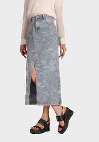 Gonna di jeans di un blu chiaro, con un motivo floreale, spacco laterale e vita alta. Abbinata a sandali con zeppa neri.