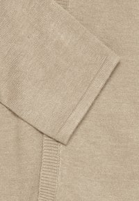 Beige kötött pulóver részlete, sima textúrával, bordázott mandzsettákkal és V-nyakú gallérral. Az anyag lágynál, enyhe fényességgel rendelkezik.