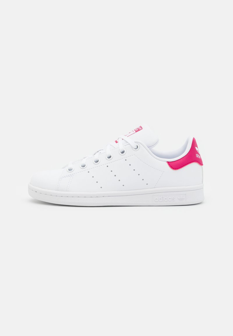 Zapatilla blanca con acento rosa en el talón, presenta un diseño perforado en los laterales y cinco ojetes para los cordones, fabricada con material sintético suave.