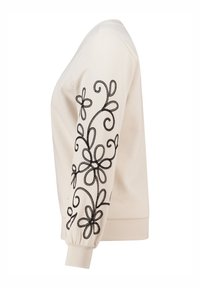 Sweatshirt crème avec broderie florale noire sur la manche gauche, bords côtes aux poignets et à l'ourlet, col rond et texture douce.