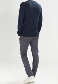 Navy knit sweater with ribbed cuffs, paired with slim-fit gray pants and white sneakers. The design features a clean, modern silhouette.