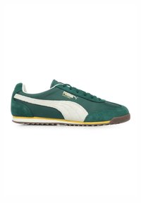 Sneaker verde in suede e tessuto con accenti bianchi, intersuola gialla e suola in gomma marrone. Presenta un design con lacci e logo Puma.
