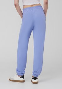 Pantaloni della tuta celesti con una vestibilità comoda, vita elastica e polsini. Indossati con scarpe da ginnastica bianche con dettagli neri.