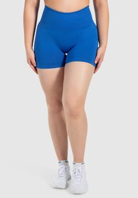Blauwe high-waisted shorts met een gladde textuur en een strakke pasvorm, voorzien van een brede tailleband en afgewerkte randen. Gepaard met witte sneakers.