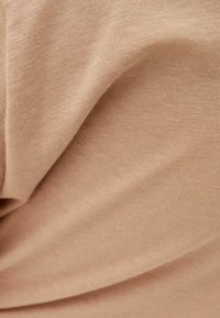 Beżowa bawełniana tkanina o gładkiej fakturze, z delikatnymi fałdami i zagnieceniami. Materiał wydaje się lekki i miękki.