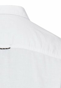 Weiße Baumwollbluse mit strukturiertem Kragen und feiner Textur. Ein kleines kariertes Etikett an der Schulterpartie setzt einen besonderen Akzent.